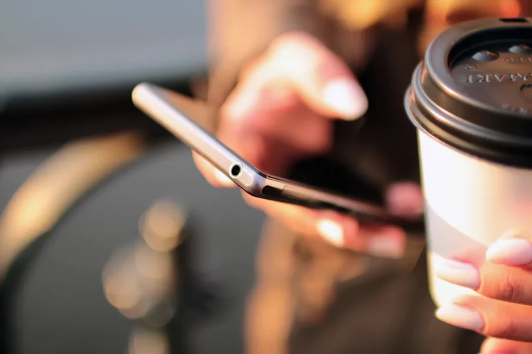 Mains tenant un smartphone, un gobelet de café à emporter au premier plan : la gestion des réseaux sociaux au quotidien