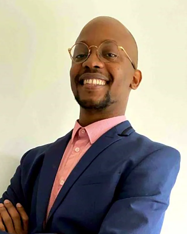 Kévin GELABALE, fondateur d'IMPAKTUS, souriant, en veste bleue et chemise rose, bras croisés