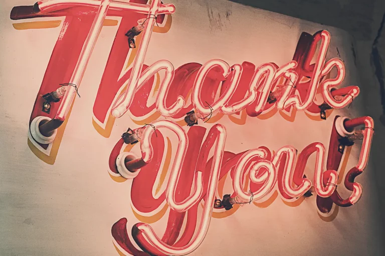 Enseigne lumineuse en néon rose « Thank you! » accrochée à un mur clair, exemple de message visible de loin