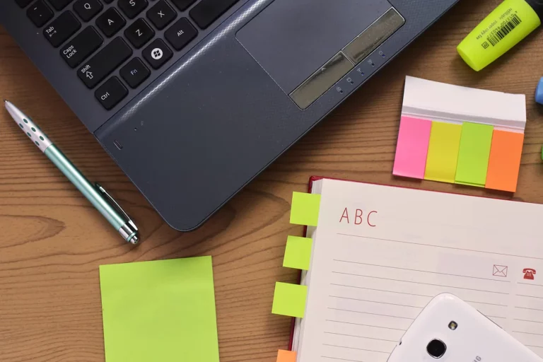 Bureau en bois avec ordinateur portable, stylo, carnet et notes repositionnables colorées : des projets en cours de préparation